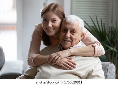 Head shot portrait smiling grownup daughter hugging older father from back, looking at camera, two generations concept, beautiful young woman embracing mature man, posing for photo together