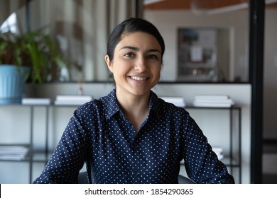 Head shot portrait smiling Indian businesswoman looking at camera, sitting in office, making video call, chatting online, business coach recording tutorial, partners internet negotiation