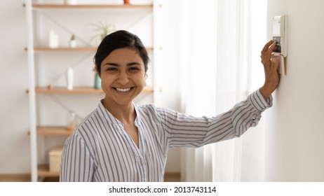 Head shot portrait of smiling Indian woman using smart home system controller on wall, happy young female looking at camera, switching temperature on thermostat or activating or turning off alarm - Shutterstock ID 2013743114