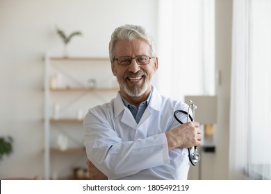 Head shot portrait smiling mature doctor holding stethoscope looking at camera, happy confident senior therapist gp wearing white uniform standing in modern office, healthcare and insurance concept - Powered by Shutterstock