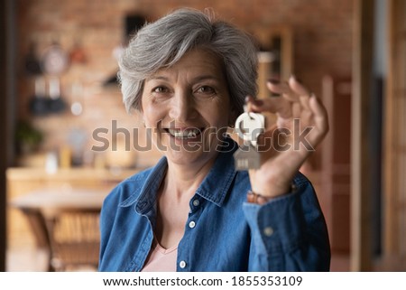 Head shot portrait smiling mature woman holding key from new home, own apartment, looking at camera, excited mature female owner moving into new house, satisfied client customer purchase real estate