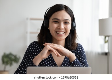 Head shot portrait of smiling millennial asian ethnicity female employee wearing modern headset with microphone, working remotely from home, communicating with colleagues by video call application.