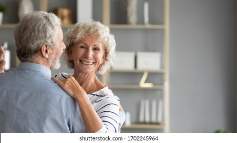 Head Shot Portrait Smiling Older Woman Dancing With Man, Happy Mature Wife And Husband Hugging, Standing In Living Room, Senior Family Enjoying Tender Moment, Celebrating Anniversary