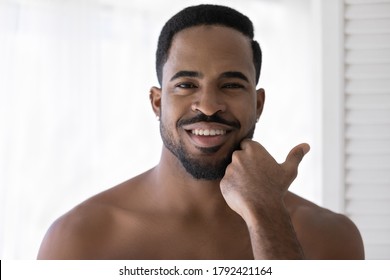Head Shot Portrait Smiling Satisfied African American Young Man Touching Beard After Shaving, Applying Aftershave Lotion Or Cream, Enjoying Skincare Procedure, Standing In Bathroom After Shower