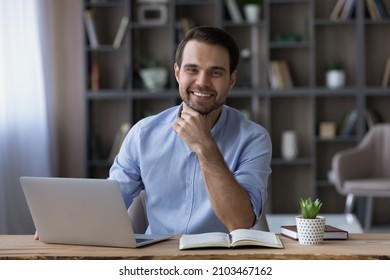 Head shot portrait of smiling successful businessman sitting at workplace desk with laptop, happy young man freelancer or student looking at camera, working or studying online, home office