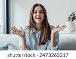 Head shot portrait smiling woman making video call to friends or relatives, using webcam, sitting on couch at home, happy young female blogger recording vlog, looking at camera, chatting online