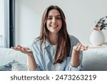 Head shot portrait smiling woman making video call to friends or relatives, using webcam, sitting on couch at home, happy young female blogger recording vlog, looking at camera, chatting online