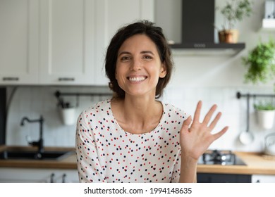 Head shot portrait of smiling woman waving hand at camera, making video call in modern kitchen at home, happy attractive young female , teacher coach recording webinar, using webcam, chatting online - Powered by Shutterstock