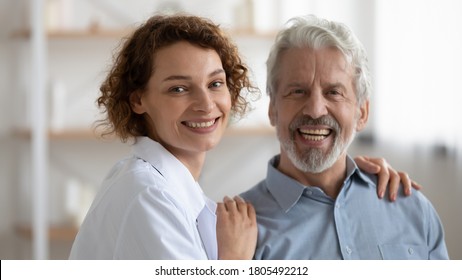 Head Shot Portrait Smiling Young Nurse Caregiver And Mature Patient Looking At Camera, Caring Woman Doctor Hugging Happy Senior Man, Touching Shoulders, Elderly Generation Healthcare Concept