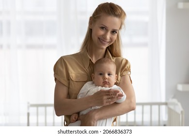 Head Shot Portrait Of Smiling Young Mother Holding Baby, Looking At Camera, Standing In Nursery At Home, Happy Mom Hugging Cute Newborn Child Infant, Posing For Family Photo, Motherhood Concept