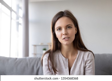 Head shot portrait young woman sitting on couch looking at camera having conversation using computer webcam modern tech talking with friend, girl recording vlog passing job interview distantly concept - Shutterstock ID 1354368368