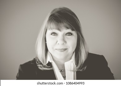 Head Shot Of Professional Business Woman In Her Upper Forties With Blonde Hair And Blue Eyes Wearing A Blue Suit Jacket, White Blouse, Necklace, Earrings And Glasses. Horizontal Landscape Orientation.