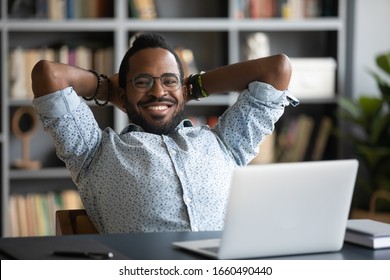 Head Shot Satisfied Calm Smiling Young African American Businessman Folded Arms Behind Head, Reclining On Chair, Relaxing, Enjoying Break Pause Time Alone In Office Or Home, Looking At Camera.