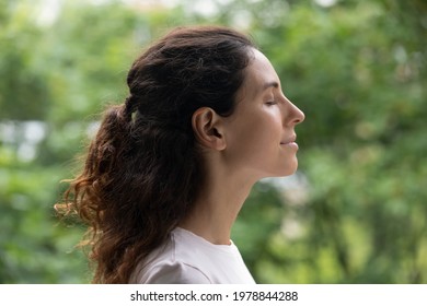 Head Shot Side View Peaceful Happy Young Hispanic Woman Standing With Closed Eyes, Breathing Fresh Air, Enjoying Stress Free Mindful Moment, Doing Yoga Relaxation Exercises, Meditating Near Nature.