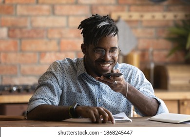 Head shot smiling 30s african businessman activating mobile application voice assistant, sitting at table at home office. Happy biracial man sending audio message, holding conversation by loudspeaker. - Powered by Shutterstock - Get 15% off with code: PIKWIZARD15