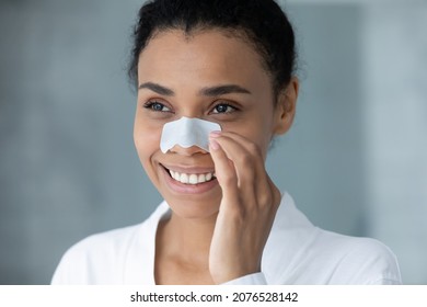 Head shot smiling attractive young african american biracial woman in bathrobe using nose cleansing strip, removing blackheads, enjoying skincare spa anti acne procedures, looking at camera. - Powered by Shutterstock