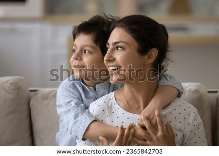 Head shot smiling dreamy Indian mother piggy backing 5s son, looking to aside in distance, visualizing good future, planning, adorable boy child hugging loving young mom, motherhood concept