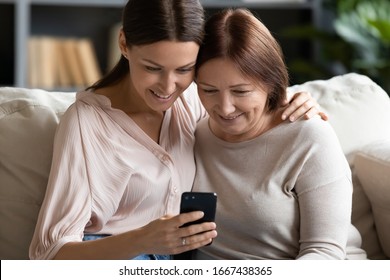 Head shot smiling grownup daughter embracing senior mature mom, posing for selfie on smartphone. Happy affectionate two female generations holding video call, using mobile applications at home.