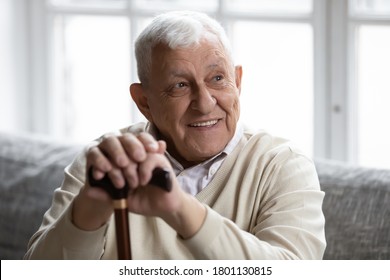 Head shot smiling old disabled man holding hands on wooden stick, resting on cozy couch in living room. Happy elderly senior grandmother recollecting good memories, enjoying relaxation time indoors. - Powered by Shutterstock