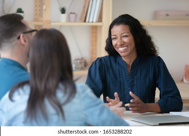 Head shot smiling professional african american financial advisor talking to clients, communicating in office. Pleasant mixed race real estate agent making good deal offer to couple at consultation.