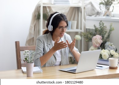 Head Shot Smiling Young Creative Businesswoman In Glasses Wearing Wireless Headphones, Enjoying Video Call Conversation With Partners Or Giving Professional Consultation To Client Online In Showroom.