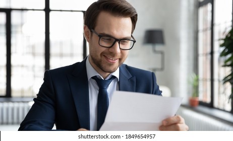 Head shot smiling young executive manager in formal wear and glasses reading pleasant news in correspondence, satisfied with project results financial report, successful worker consider paper document