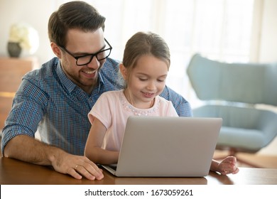 Head shot smiling young father in eyeglasses cuddling small preschool daughter, watching funny video on computer. Happy single dad shopping online on laptop with adorable little child girl at home.