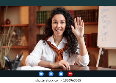 Head shot of smiling young female teacher waving hand to webcam, greeting students during remote lecture or online course, using computer video call software application, laptop screen view