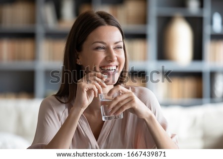Head shot smiling young woman holding pill and glass of fresh pure water. Healthy millennial lady taking antioxidant medicine vitamins, beauty supplements for hair skin nails, healthcare concept.
