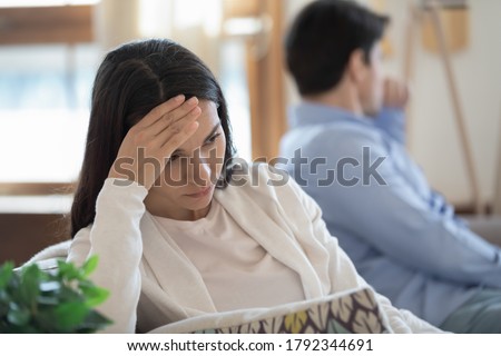 Head shot stressed confused young mixed race woman sitting in sofa separately with offended husband, ignoring each other after conflict quarrel, marriage relationship misunderstanding problem.