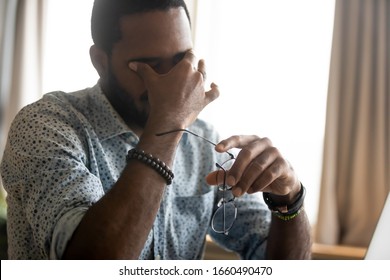 Head Shot Stressed Young Multiracial Businessman Massaging Eyes, Suffering From Painful Feelings. Exhausted African Ethnicity Man Having Problems With Vision, Blurred Eyesight Due To Overwork.