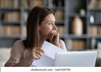 Head shot stressed young woman holding paper document, bank debt notification, thinking of financial troubles, looking away. Lost in negative thoughts depressed woman worrying about bad news notice.