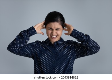 Head shot stubborn annoyed Indian woman plugging with fingers covering ears on grey studio background isolated, unhappy irritated businesswoman or student with closed eyes ignoring loud noise sound