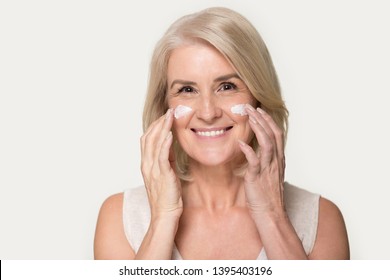 Head Shot Studio Portrait Attractive Mature Blond Woman Look At Camera Gently Touch Face Apply Moisturizing Or Anti-aging Wrinkle Serum Cream, Natural Beauty Skin Care Concept Image On Grey Background