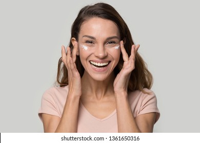 Head shot studio portrait happy attractive woman looking at camera having white shiny smile, gently touch face apply eyelid moisturizing cream anti age wrinkle serum, natural beauty, skin care concept