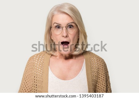 Head shot studio portrait mid age amazed mature woman in glasses open mouth gawp look at camera feels stunned isolated on grey background, shocking news, crazy discount sale, terrible happened concept