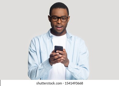 Head shot surprised African American man looking at phone screen, young male using cellphone, reading unexpected good news in email, online win, shopping discount offer, isolated on grey background