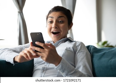 Head shot surprised young indian girl looking at phone screen. Amazed overjoyed millennial hindu woman reading sms with unexpectable unbelievable news with opened mouth, online lottery win concept.
