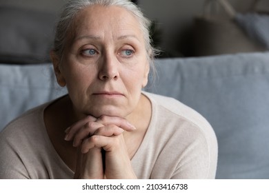 Head shot thoughtful old senior grandmother looking in distance, suffering from loneliness or psychological problems, recollecting bad memories, having nostalgic mood sitting on couch at home. - Shutterstock ID 2103416738