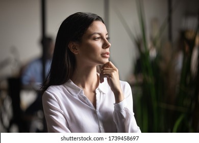 Head shot thoughtful young businesswoman touching chin, looking in distance, dreaming about future, project strategy, pensive female intern pondering startup ideas, standing in office
