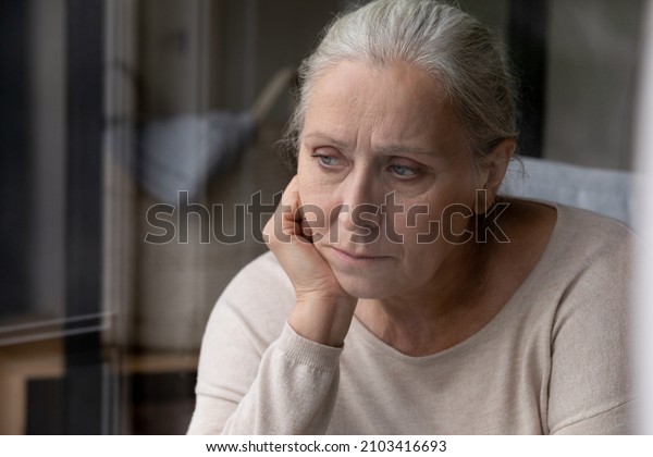 Head shot unhappy confused middle aged elderly\
retired woman looking in distance suffering from loneliness at\
home, remembering life moments, recollecting memories, thinking of\
psychological troubles.