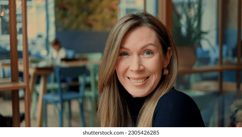 Head shot woman raise eyebrows smile openly in urban cafe with genuine interior. Straight camera look of cheerful lady with long light brown hair in city restaurant. High quality photo - Powered by Shutterstock