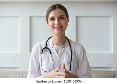 Head Shot Of Woman Wearing White Coat Stethoscope On Shoulders Looking At Camera, Doctor Make Video Call Interact Through Internet Talk With Patient Provide Help Online Counseling And Therapy Concept