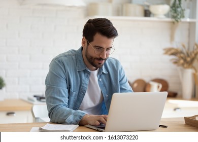Head shot young businessman sitting at table with computer, working remotely, writing email or reading news. Young man attending distant educational courses, planning job or communicating online. - Shutterstock ID 1613073220
