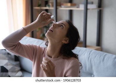 Head shot young caucasian woman using medical eyes drops suffering from dry eyes syndrome or curing ophthalmology disease at home. Unhealthy millennial lady having blurred eyesight, treating eyes.