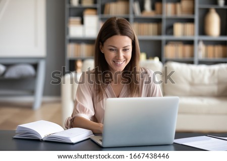 Head shot young happy woman sitting at desk, working on computer at home. Pleasant attractive smiling lady looking at laptop screen, shopping, chatting in social networks, studying online remotely.