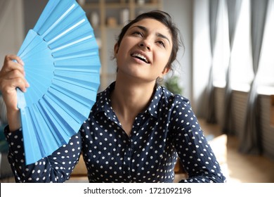 Head shot young indian woman using blue paper fan, feeling hot relieved indoors. Sweaty millennial hindu girl teenage cooling herself, breathing fresh air, spending time at home without conditioner. - Shutterstock ID 1721092198