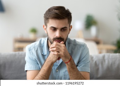 Head Shot Young Millennial Serious Man Sitting On Couch Home. Portrait Of Thoughtful Pensive Handsome Serious Male Student Thinking About New Idea Project Analysing Planning Making Decision Concept