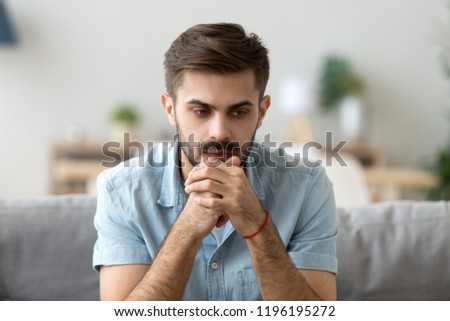 Head shot young millennial serious man sitting on couch home. Portrait of thoughtful pensive handsome serious male student thinking about new idea project analysing planning making decision concept