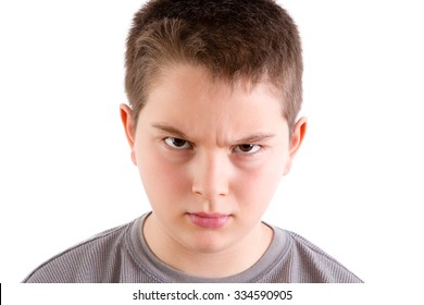 Head And Shoulders Close Up Portrait Of Young Boy Looking At Camera With Stern And Disapproving Expression And Furrowed Brow In Front Of White Background